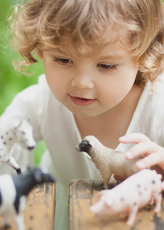 Engaged kid playing with farm animal figurines at a park.