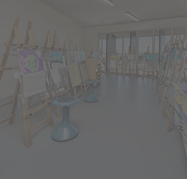 Greyed out image of art classroom with easels, canvases, stools and art supplies.