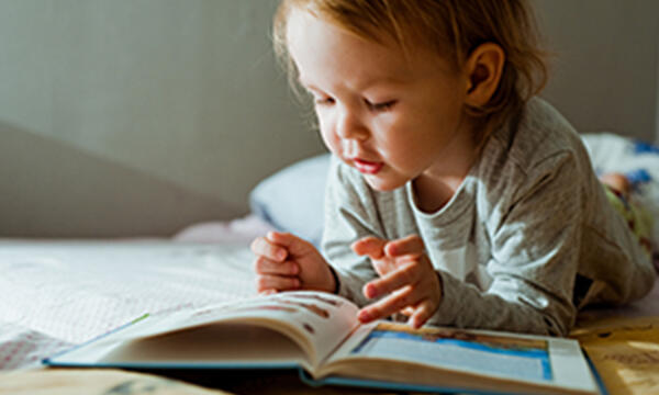 Toddler reading a book in bed.